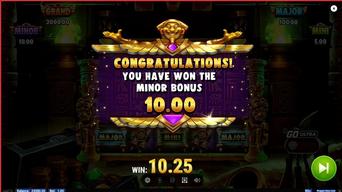 Tampilan visual slot Wrappin’ More Gold dengan karakter mumi yang ramah dan latar belakang harta karun Mesir.